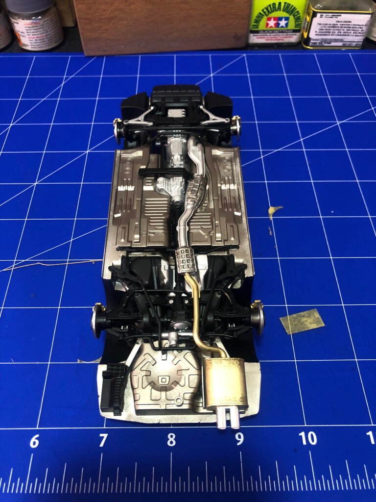 Visão inferior do chassi montado do Nissan Skyline GT-R Tamiya 1/24 com sistema de escapamento e transmissão detalhados.