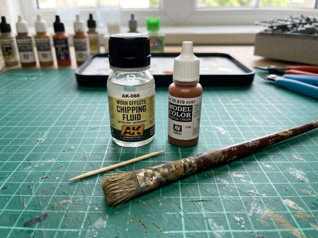 Materiais para técnica de efeito chipping facil organizados na bancada: frasco de fluido de desgaste, tinta acrílica de ferrugem, pincel de cerdas duras e palito
